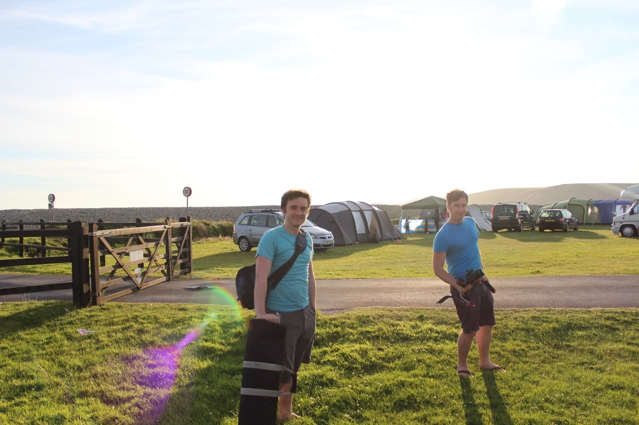 Eifion and Martin with camera kit at the gate of Newgale Camp Site in Pembrokeshire, golden hour