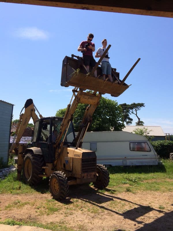 Two of the crew filming from the raised bucket of a farm digger